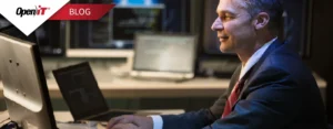 a professional in a suit working on a laptop in a control room environment with multiple monitors. represents open it’s software license inventory management, emphasizing monitoring, tracking, and optimization of software licenses for enterprise use.